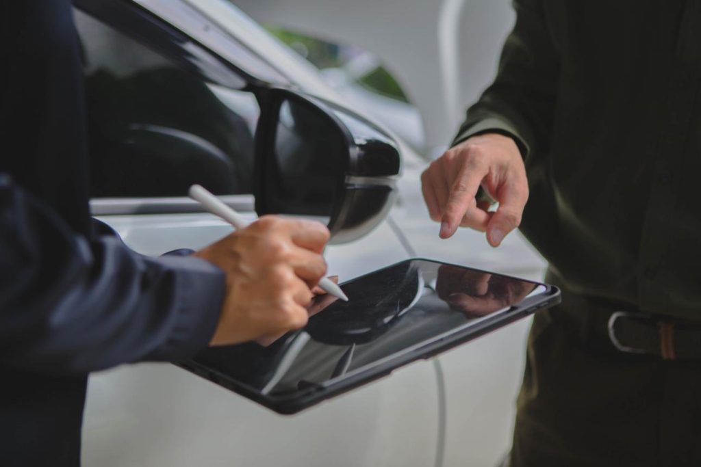 Persona apuntando algo en una tablet al lado de un coche