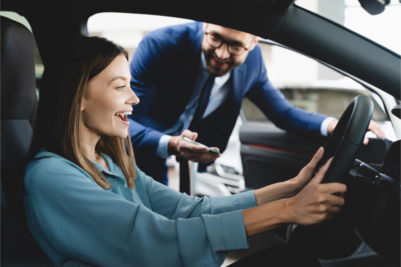 Mujer sonriente al volante y hombre de traje al lado